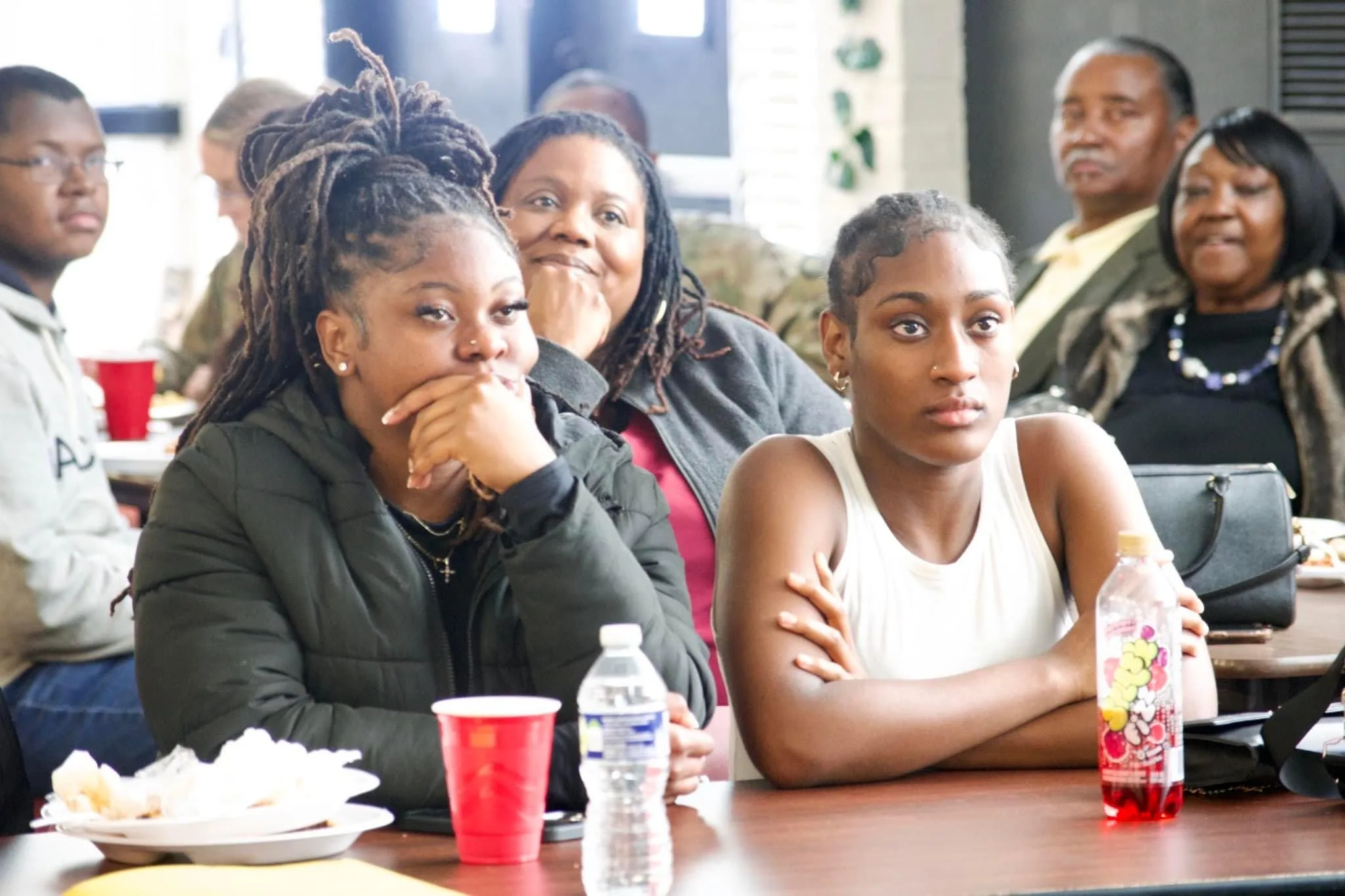 MIAC- students two girls sitting beside each other with parents behind them